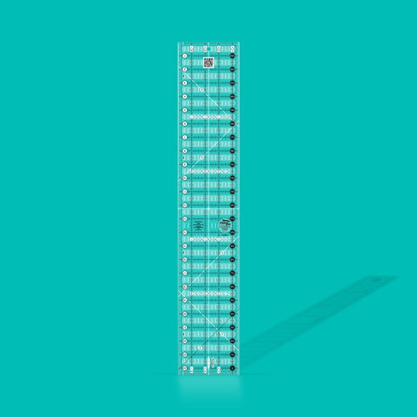 Creative Grids Quick Trim Two 4.5-inch by 24.5-inch long acrylic ruler laid across a folded bolt of fabric.