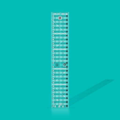 Creative Grids Quick Trim Two 4.5-inch by 24.5-inch long acrylic ruler laid across a folded bolt of fabric.