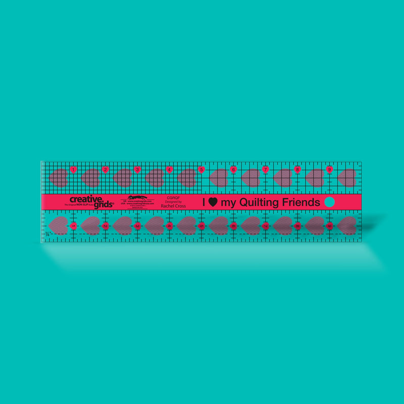 Creative Grids I Love My Quilt Friends 2.5-inch by 10-inch rectangle ruler with pink accents laid over jelly roll fabric strips.