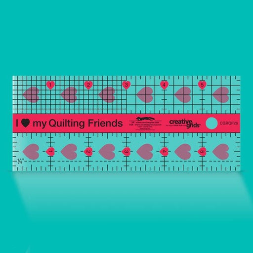 Creative Grids I Love My Quilt Friends Mini 2.5-inch by 6-inch rectangle ruler with pink accents laid over a small patchwork block.