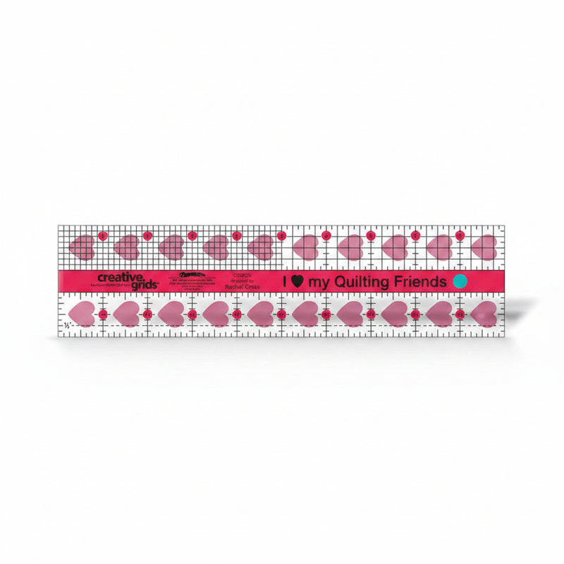 Creative Grids I Love My Quilt Friends 2.5-inch by 10-inch rectangle ruler with pink accents laid over jelly roll fabric strips.