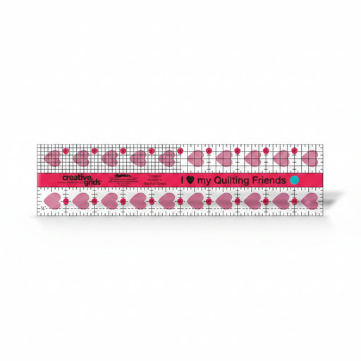 Creative Grids I Love My Quilt Friends 2.5-inch by 10-inch rectangle ruler with pink accents laid over jelly roll fabric strips.