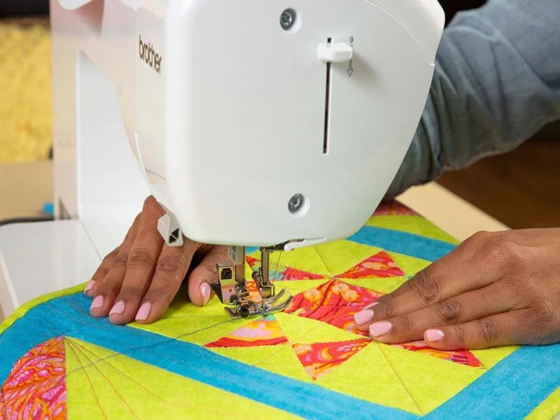 close-up-hands-guiding-bright-green-and-orange-geometric-quilt-top-under-brother-pacesetter-innov-is-ps700-needle