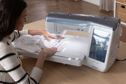 side-angle-view-woman-guiding-white-garment-under-brother-celeste-innov-is-cx1-sewing-machine-needle