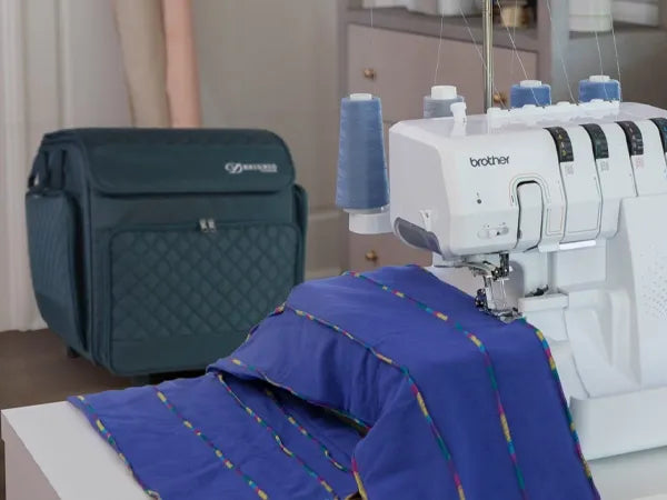 brother-airflow-3000-air-serger-stitching-blue-fabric-on-table-next-to-wheeled-carrying-case