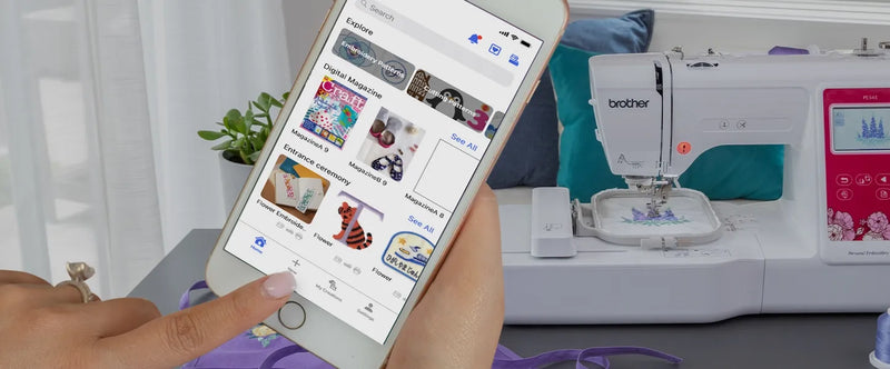 user-hand-holding-smartphone-displaying-artspira-mobile-app-interface-next-to-brother-pe545-embroidery-machine
