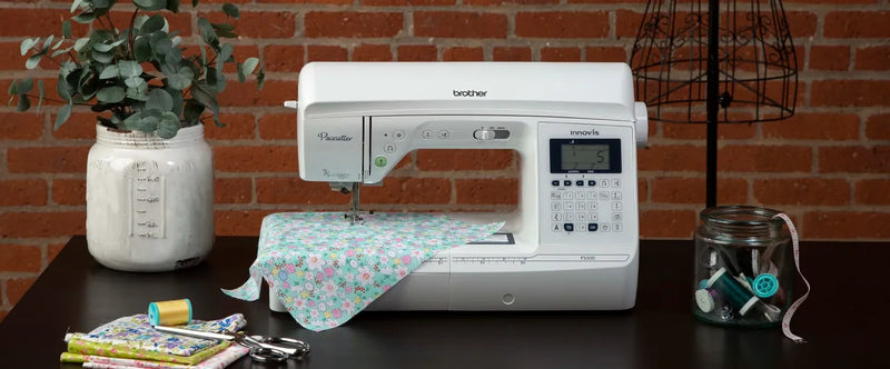 brother-pacesetter-innov-is-ps500-sewing-machine-on-dark-table-with-floral-fabric-and-notions