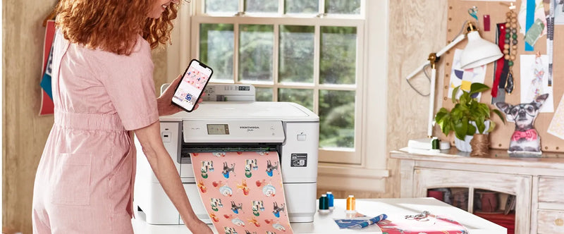 woman-holding-smartphone-displaying-artspira-app-interface-next-to-brother-printmoda-studio-fabric-printer-hl-jf1
