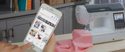 user-hand-holding-smartphone-displaying-artspira-app-interface-next-to-brother-se2000-machine