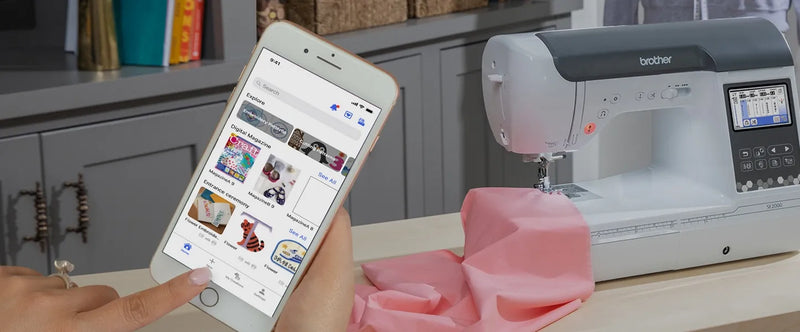user-hand-holding-smartphone-displaying-artspira-app-interface-next-to-brother-se2000-machine