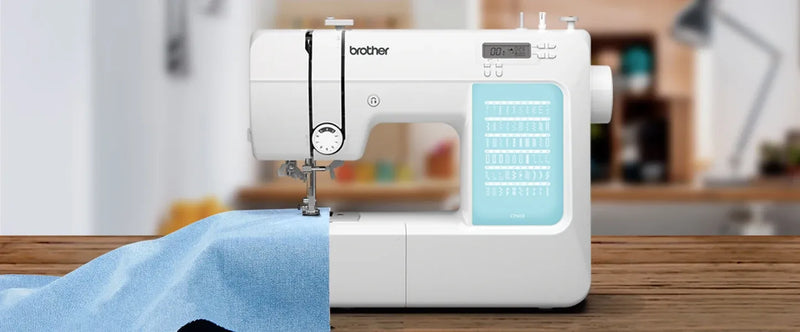 brother-cp60x-computerized-sewing-machine-lifestyle-view-feeding-light-blue-fabric-on-wooden-table
