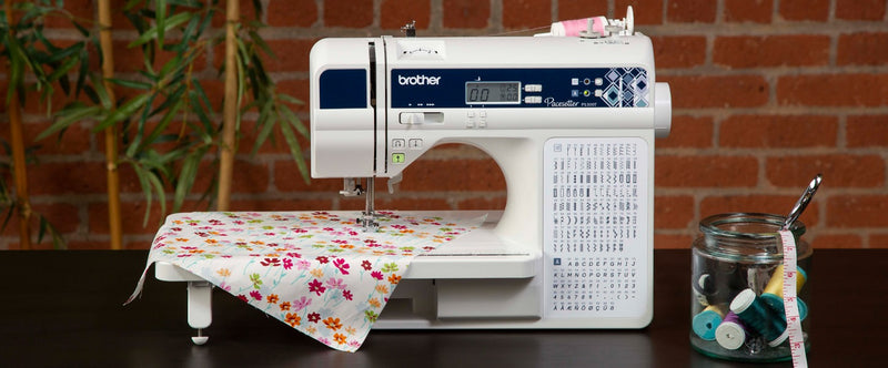 brother-pacesetter-innov-is-ps300t-sewing-and-quilting-machine-on-dark-table-with-floral-fabric-and-thread-spools-jar